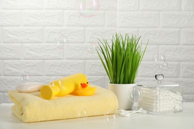 Baby bath accessories. Towel, cosmetic products, cotton swabs and toy duck on white table against brick wall