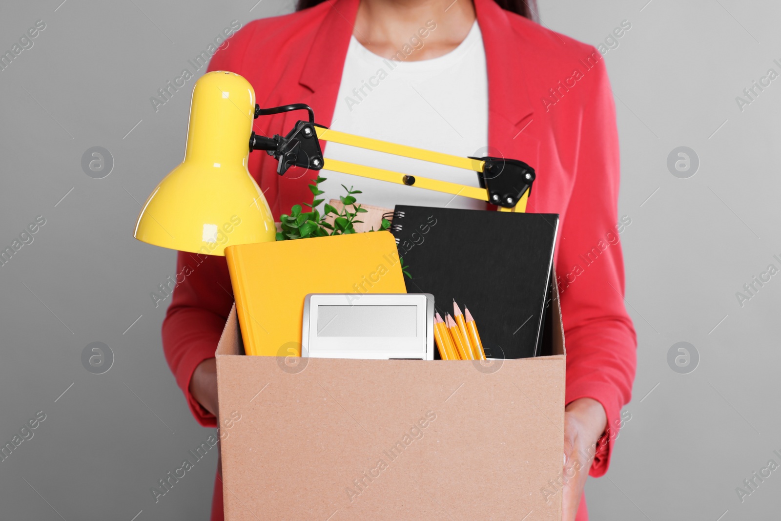 Photo of Unemployed woman with box of personal office belongings on grey background, closeup