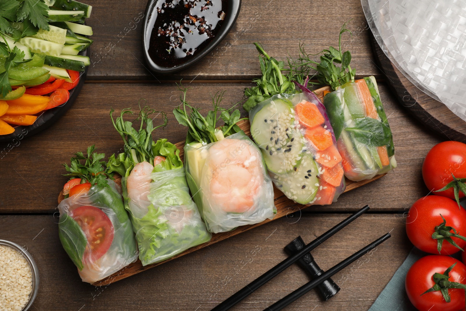 Photo of Many different delicious rolls wrapped in rice paper on wooden table, flat lay