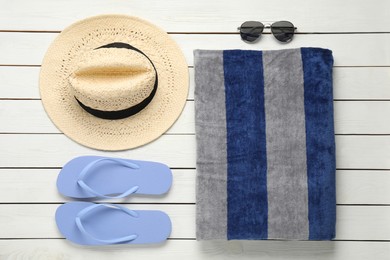 Beach towel, flip flops, hat and sunglasses on white wooden background, flat lay