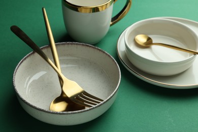 Stylish empty dishware and golden cutlery on green background