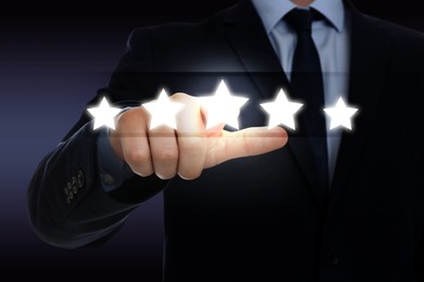 Image of Quality rating. Man pressing on star on virtual screen against dark background, closeup