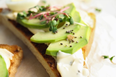 Photo of Tasty toast with avocado, sprouts and chia seeds on parchment, closeup