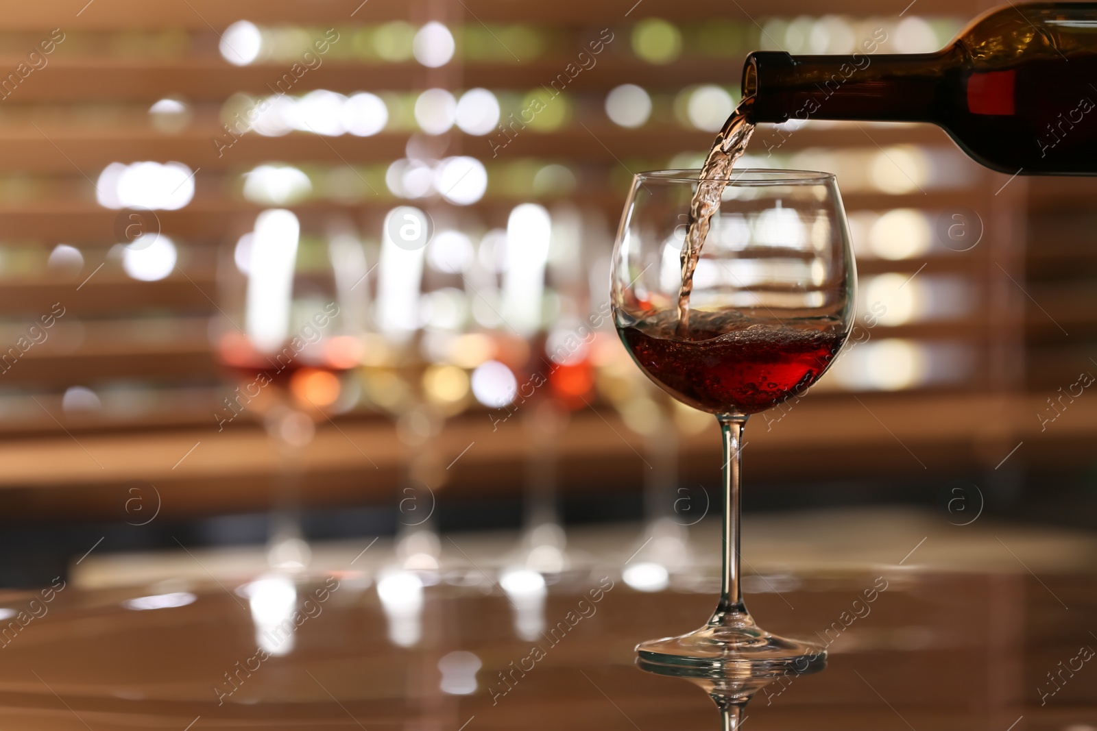 Photo of Pouring rose wine from bottle into glass on table against blurred background, space for text