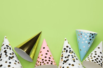 Bright party hats on light green background, flat lay. Space for text