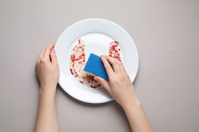 Photo of Woman washing dirty plate with sponge on light grey background, top view