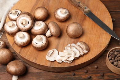 Photo of Cutting board with fresh champignon mushrooms and knife on wooden table