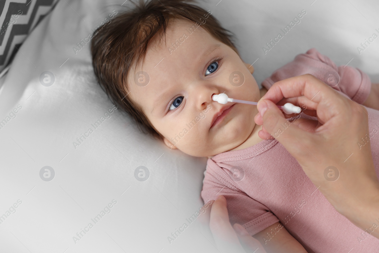 Photo of Mother cleaning nose of her baby with cotton bud on bed, top view