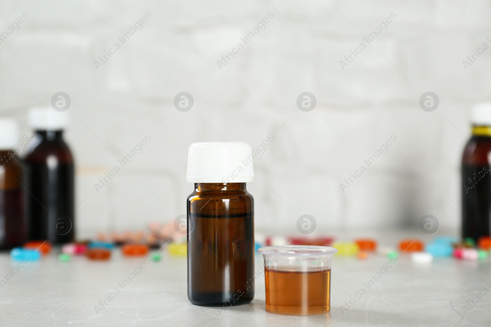 Photo of Bottle of cough syrup and measuring cup on light grey table. Space for text
