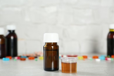 Bottle of cough syrup and measuring cup on light grey table. Space for text