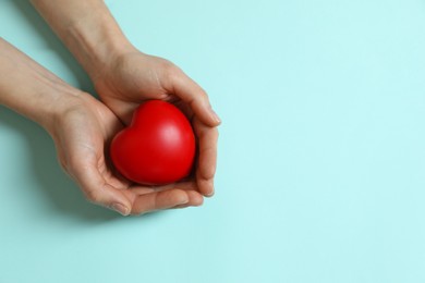 Photo of Woman holding red decorative heart on light blue background, top view. Space for text