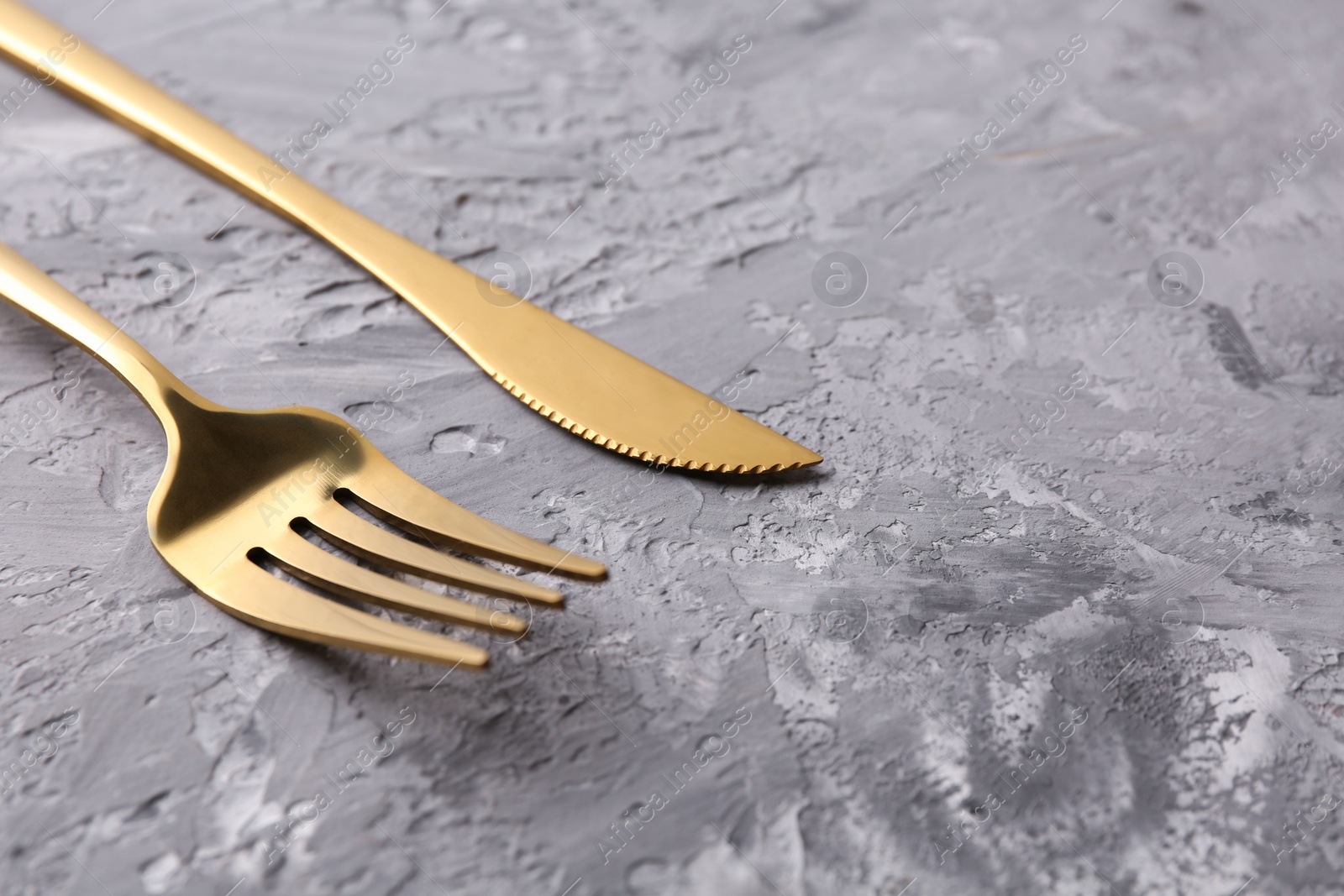 Photo of Stylish cutlery. Golden knife and fork on grey textured table, closeup. Space for text
