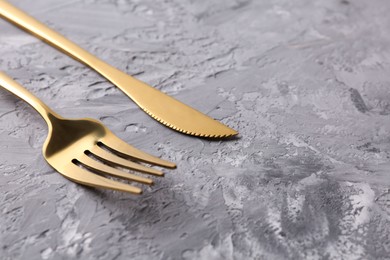 Stylish cutlery. Golden knife and fork on grey textured table, closeup. Space for text