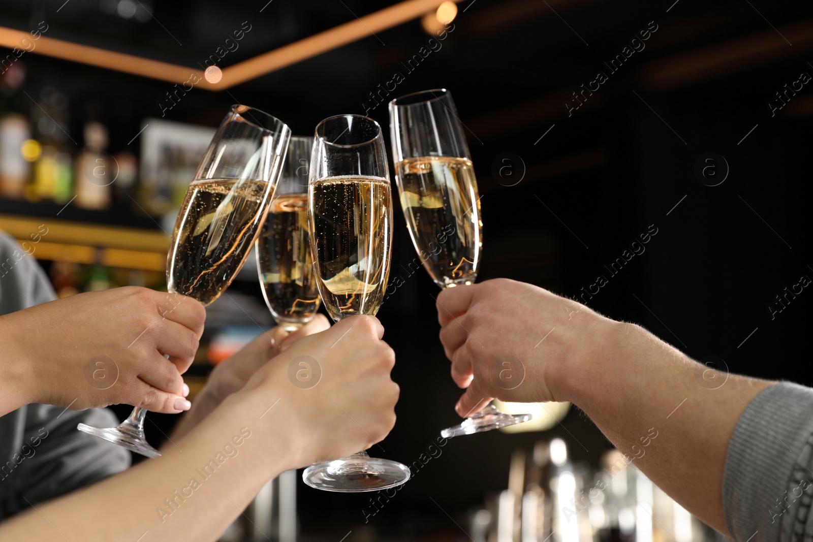 Photo of Friends clinking with glasses of champagne in bar, closeup