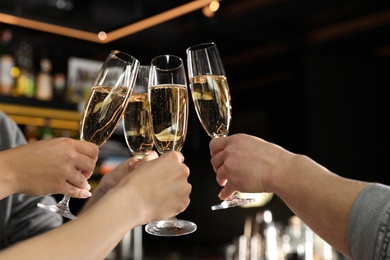 Friends clinking with glasses of champagne in bar, closeup