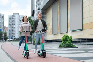 Photo of Happy couple riding modern electric kick scooters on city street, space for text
