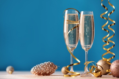 Photo of Glasses of champagne with serpentine streamers and Christmas ornaments on table against blue background