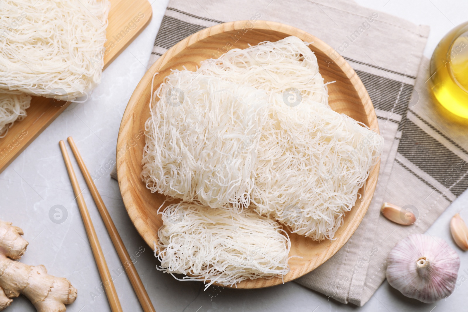 Photo of Wooden bowl with uncooked rice noodles on light grey table, flat lay