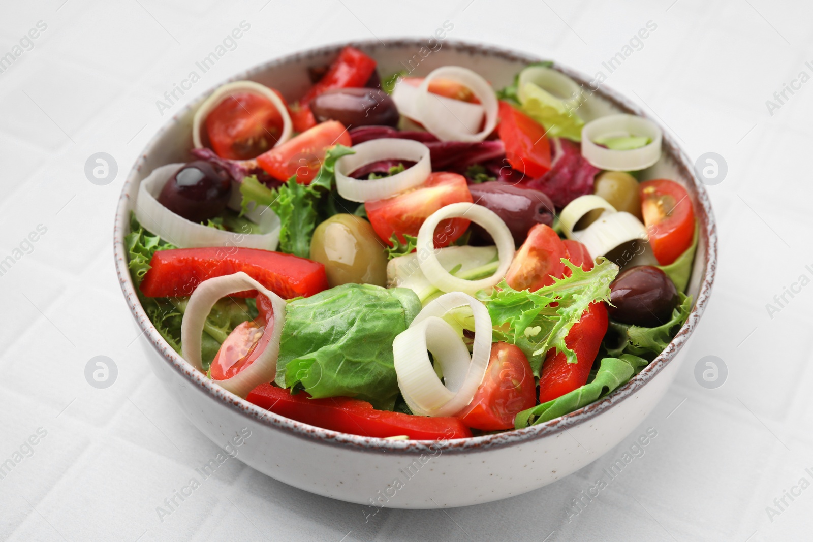 Photo of Bowl of tasty salad with leek and olives on white tiled table, closeup