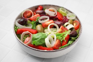 Bowl of tasty salad with leek and olives on white tiled table, closeup