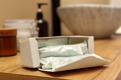 Photo of Package of tampons on wooden countertop in bathroom, closeup. Menstrual hygienic product