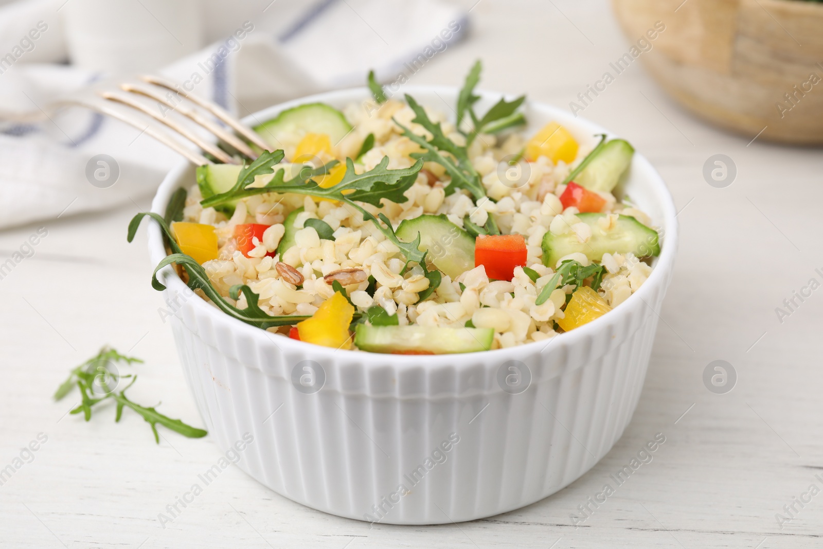 Photo of Cooked bulgur with vegetables in bowl on white wooden table, closeup