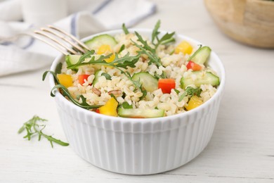 Cooked bulgur with vegetables in bowl on white wooden table, closeup