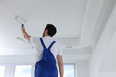 Handyman with roller painting ceiling in room, back view