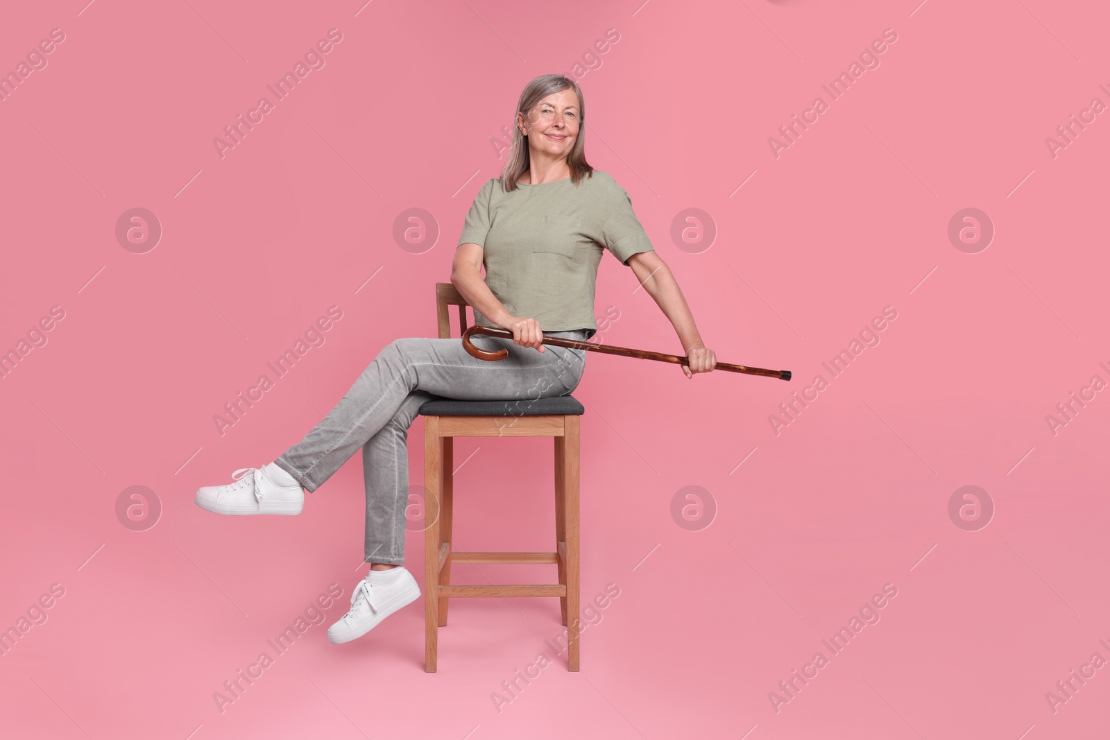 Photo of Senior woman with walking cane sitting on chair against pink background