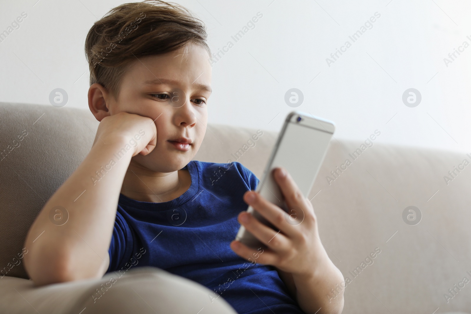 Photo of Little child with smartphone on sofa in room. Danger of internet