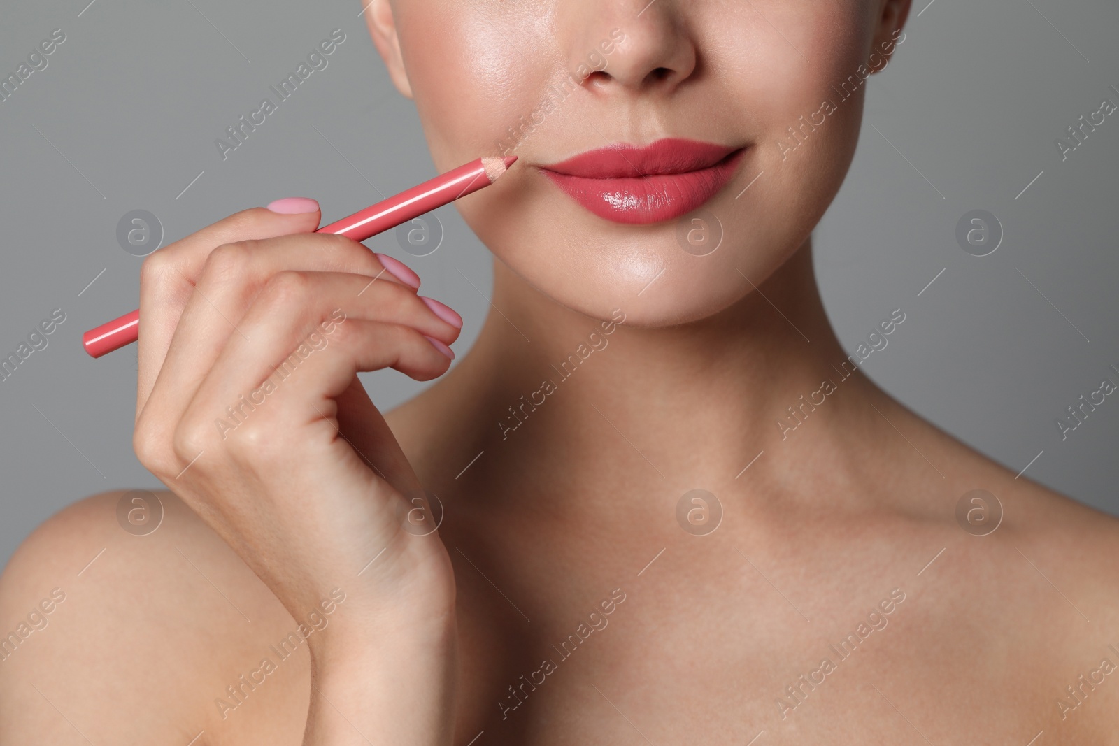 Photo of Young woman with beautiful pink lip pencil on grey background, closeup
