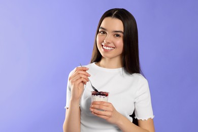 Photo of Happy teenage girl with delicious yogurt and spoon on violet background. Space for text