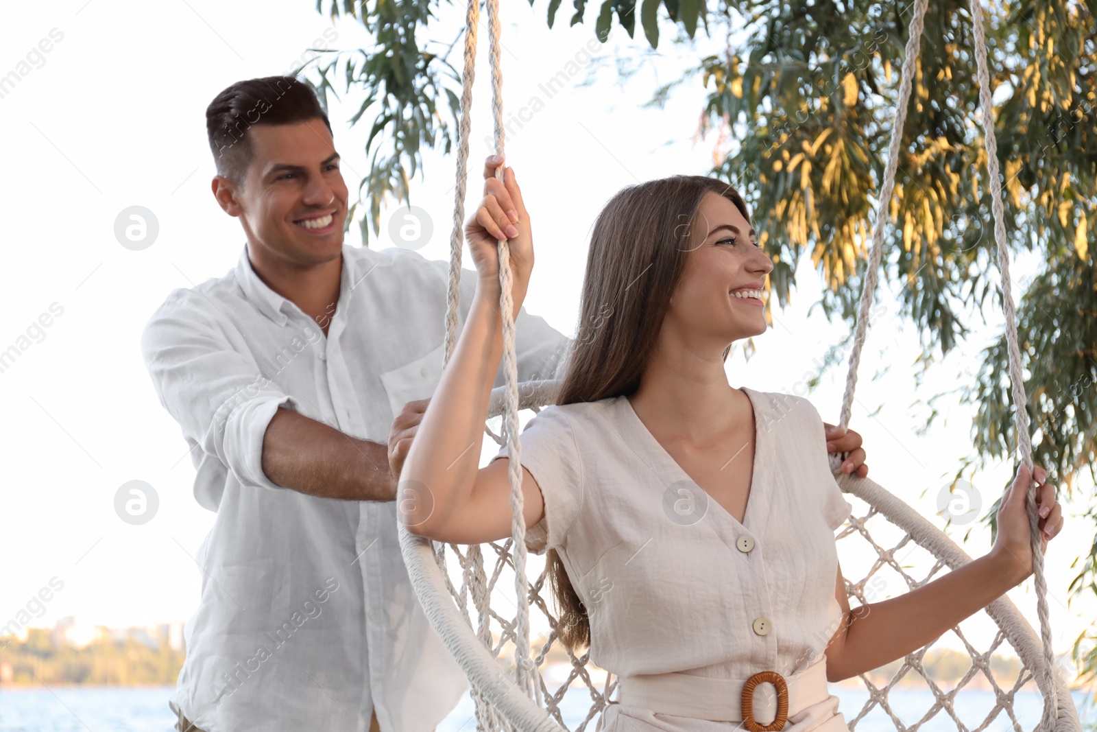 Photo of Young woman in hammock chair and her boyfriend on beach. Summer vacation