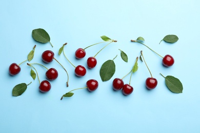 Photo of Tasty ripe cherries with leaves on light blue background, flat lay