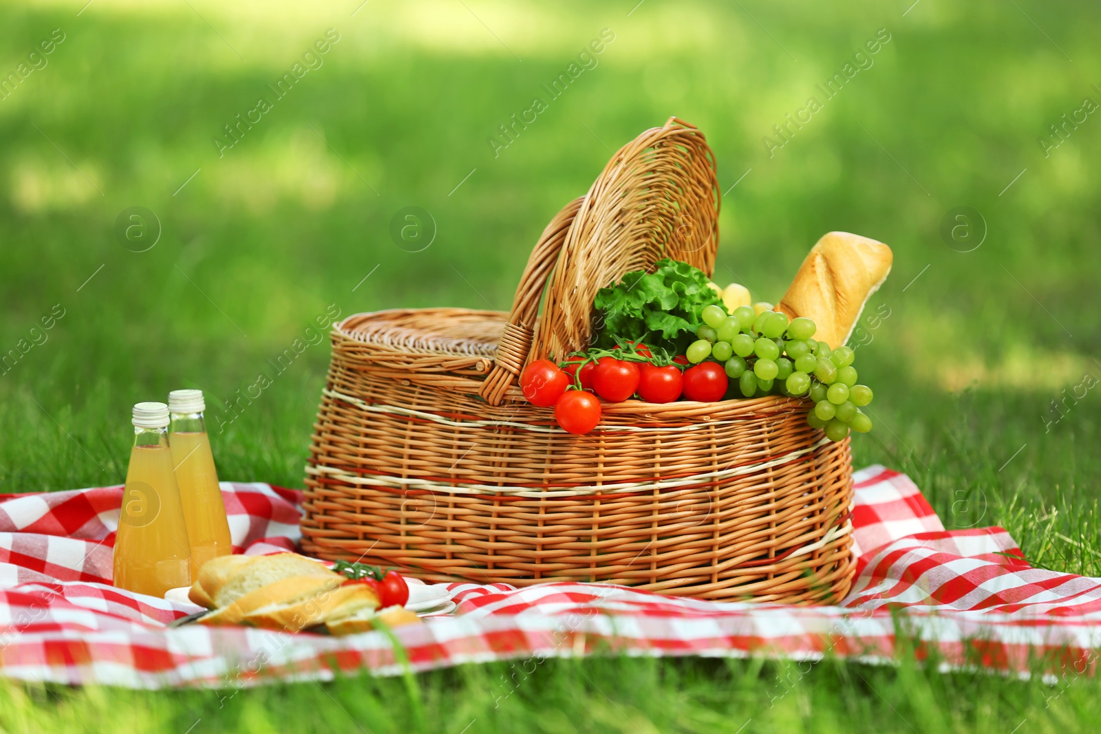 Photo of Wicker basket with food and juice on blanket in park. Summer picnic
