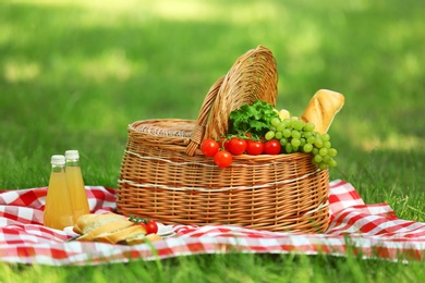 Wicker basket with food and juice on blanket in park. Summer picnic