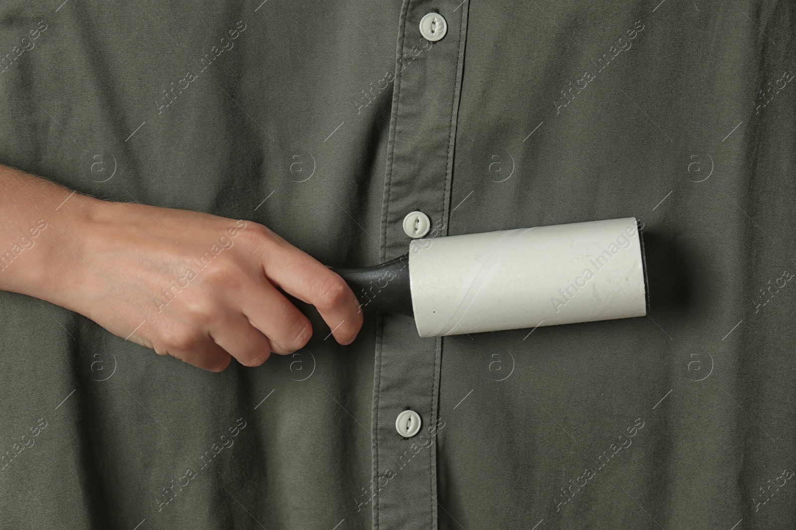 Photo of Woman cleaning khaki shirt with lint roller, closeup