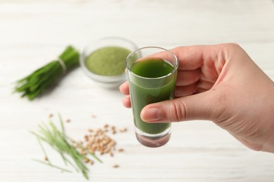 Photo of Woman holding glass of wheat grass drink at white table, closeup