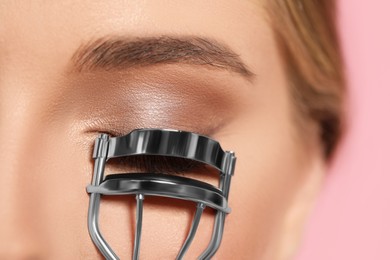 Photo of Young woman with eyelash curler on pink background, closeup
