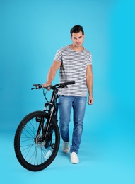 Handsome young man with modern bicycle on light blue background