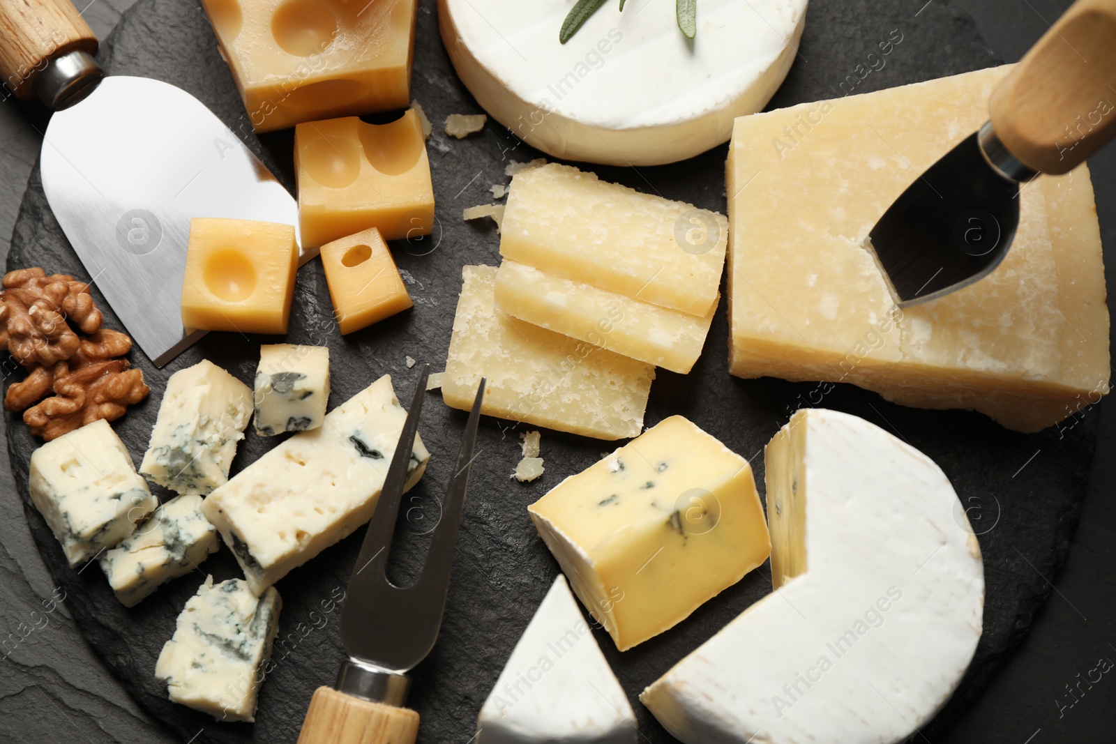 Photo of Cheese platter with specialized knives and fork on black table, flat lay