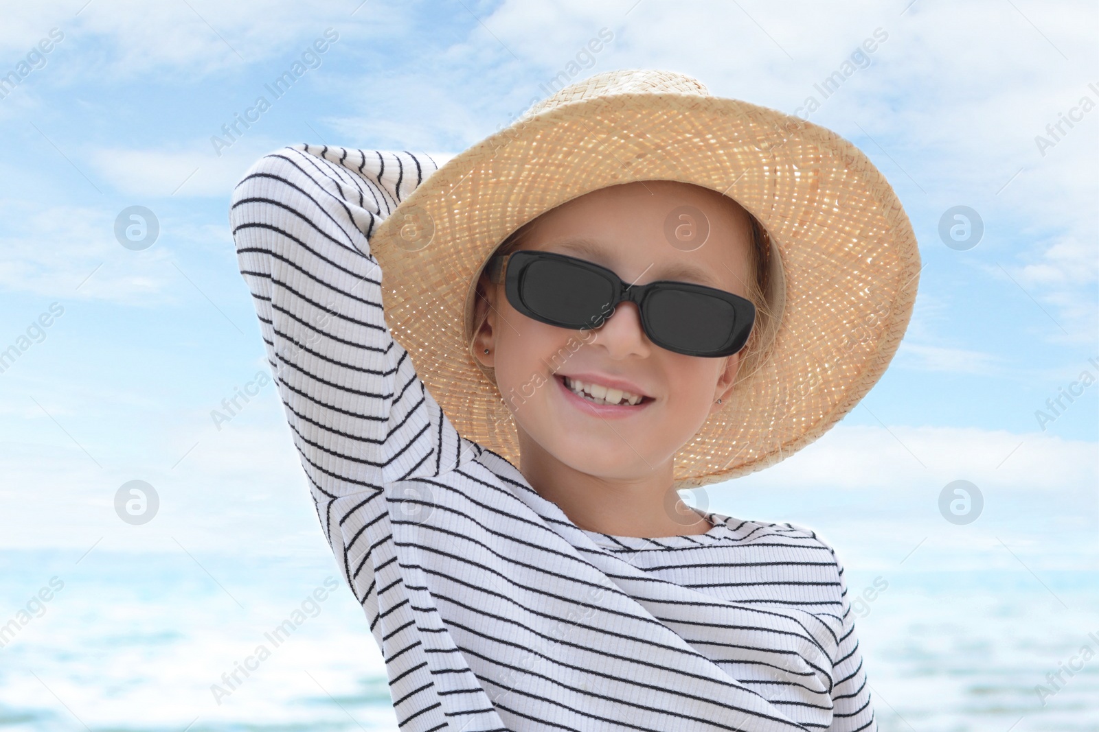 Photo of Little girl wearing sunglasses and hat at beach on sunny day