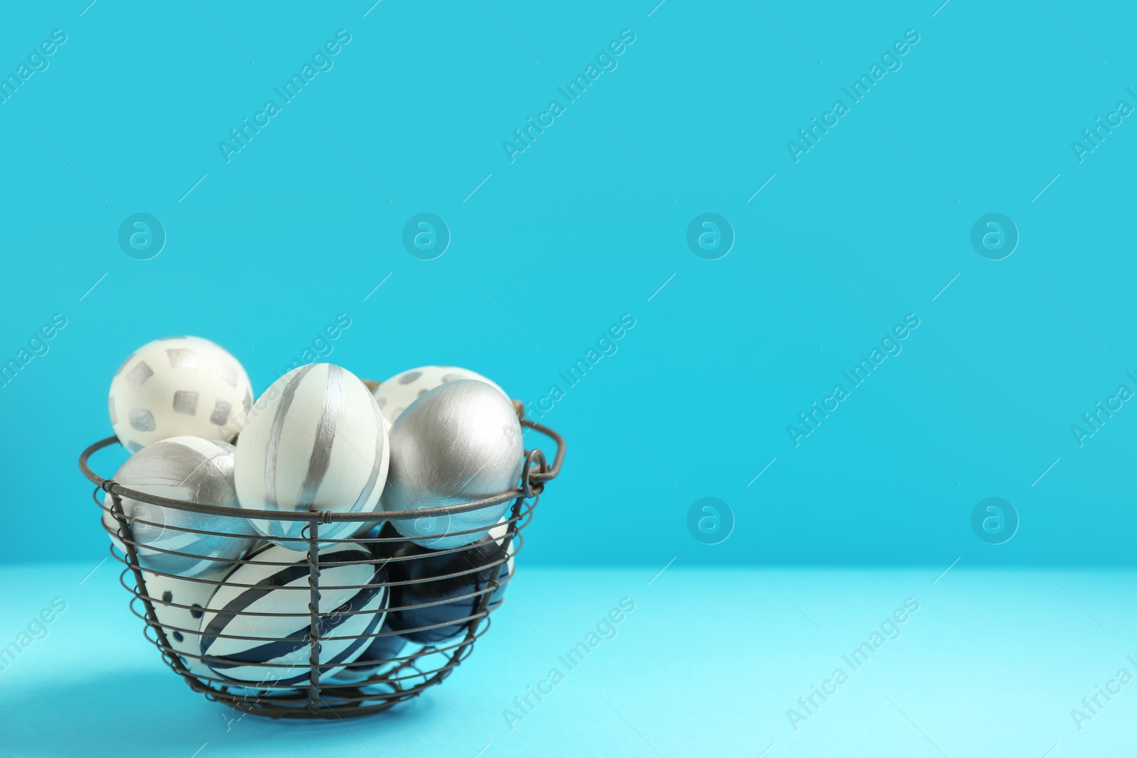 Photo of Basket full of painted Easter eggs on color background, space for text