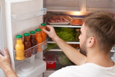 Photo of Young man taking bottle of juice from refrigerator in kitchen