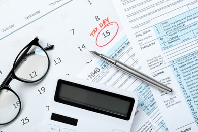 Tax day. Calendar with date reminder, documents, pen, glasses and calculator on table, flat lay