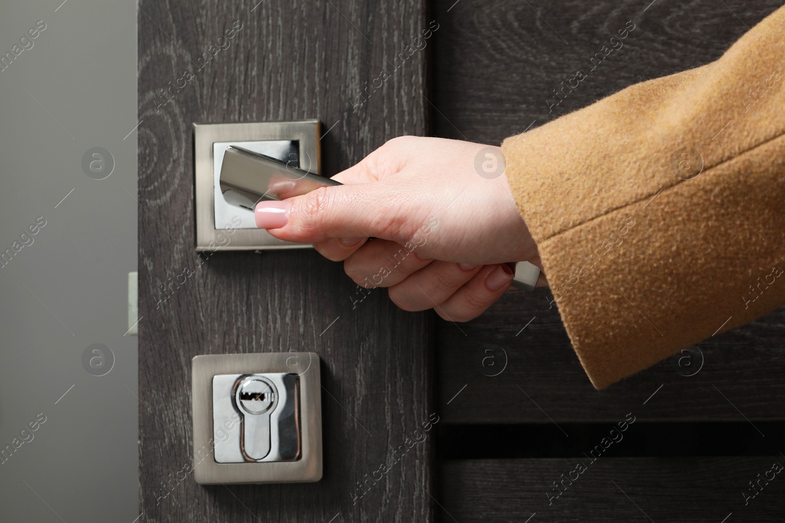 Photo of Woman opening wooden door indoors, closeup of hand on handle