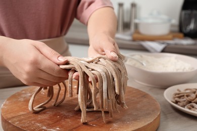 Photo of Woman making soba (buckwheat noodles) at wooden table in kitchen, closeup