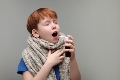 Photo of Little boy with scarf using throat spray on grey background