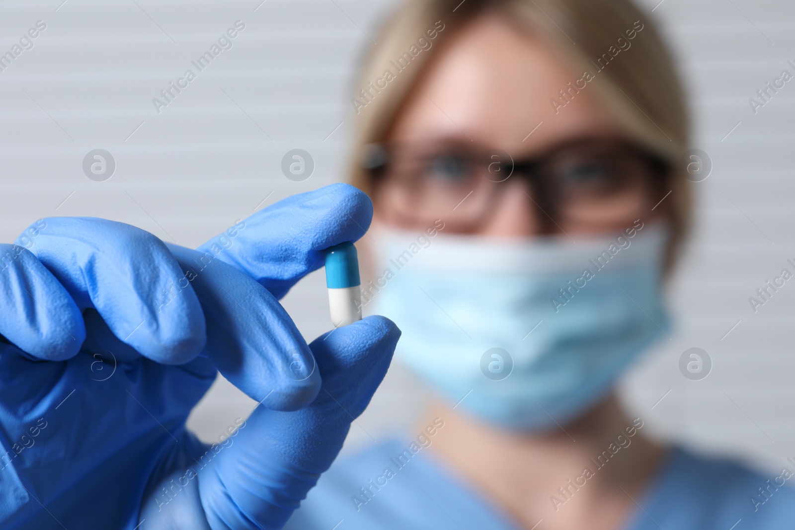 Photo of Doctor holding pill on light background, selective focus. Space for text