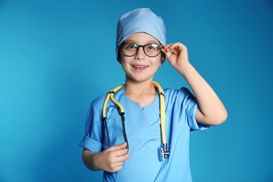 Photo of Cute little child in doctor uniform with stethoscope on color background